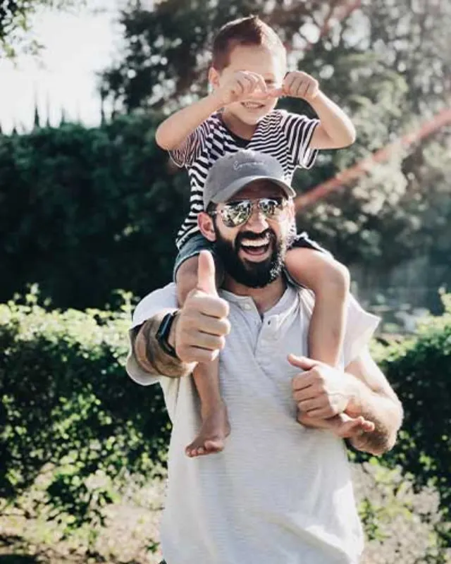 A smiling father carrying his young child on his shoulders